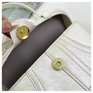 Detail of the golden magnetic buckle closure on a quilted white crossbody box bag