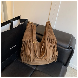 Close-up of bohemian dark brown suede shoulder bag featuring long fringe and gold buckle