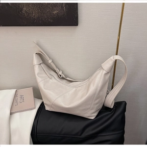 Detail of a creamy white half-moon shoulder bag with diagonal stitching and wide strap