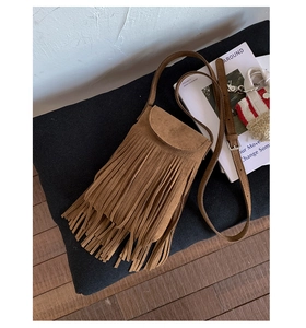 Détail du sac bandoulière en daim marron avec franges multicouches sur un sol en bois