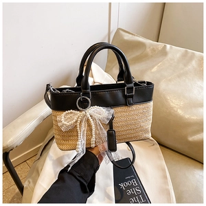 Close-up of straw tote bag with black leather trim and pearl lace bow charm detail