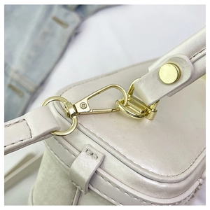 Detail view of pearlescent white mini box bag with golden lobster clasp and hardware