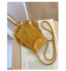 Vue détaillée du sac bandoulière en daim jaune moutarde avec franges sur des livres