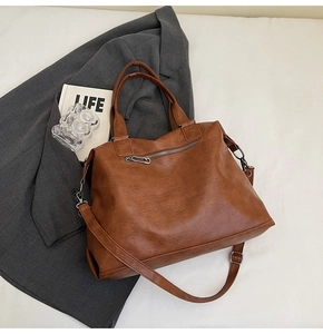 Brown soft leather tote bag detail with metal zipper and adjustable strap on office desk