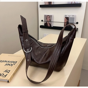 Detail of dark brown glossy leather dumpling bag with silver buckle and smooth zipper