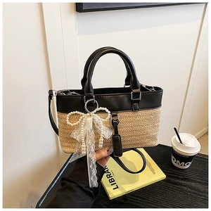 Detail view of woven straw tote bag with black PU leather trim and pearl lace bow