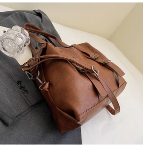 Detailed view of a vintage brown leather tote bag resting on a grey blazer with modern accents