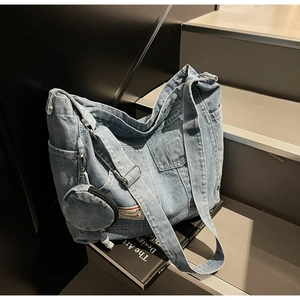 Detail of blue wash denim tote bag showing wide shoulder strap and round coin purse accessory