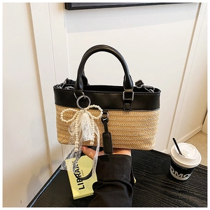 Detail of straw woven tote with black leather trim and pearl bow charm accessory