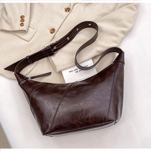 Close-up of a dark brown crescent bag with oily leather texture and wide shoulder strap