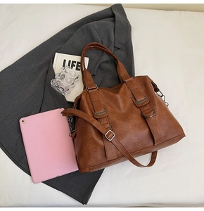 Detail of caramel brown leather tote bag with metallic buckles and adjustable shoulder strap