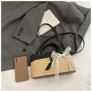 Detail of straw woven tote bag featuring black leather trim and elegant pearl bow accents