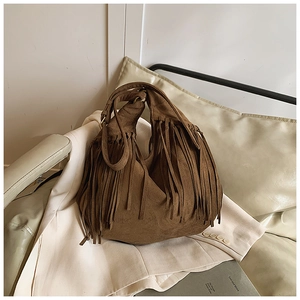 Detailed view of brown suede bohemian hobo bag with long fringe on a beige blazer background