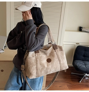 Dettaglio borsa da viaggio in tela beige con manici in pelle marrone e logo tondo