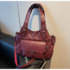 Detail of burgundy textured leather tote bag with front flap pocket on a leather sofa