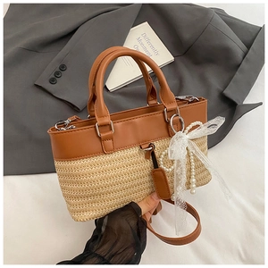 Detail of straw tote bag featuring leather trim, pearl charm, and lace bow decoration