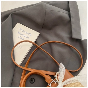 Detail of woven straw tote with brown leather handles and decorative lace pearl bow