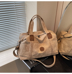 Dettaglio della borsa da viaggio kaki con logo in pelle e doppi manici sulla scrivania