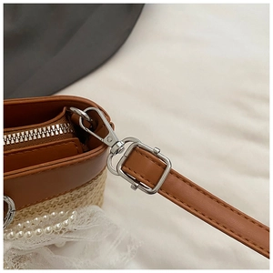 Detail of straw woven tote showing brown leather strap, silver buckle and lace pearls