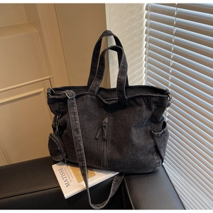 Detail of dark denim tote bag with front zipper pocket and adjustable strap in soft light