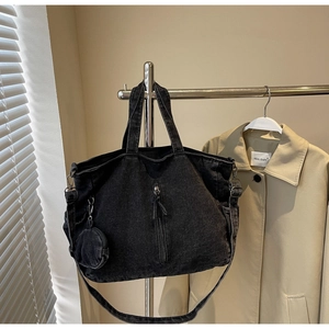Detail of black denim tote bag featuring vertical zip pocket and round coin purse attachment