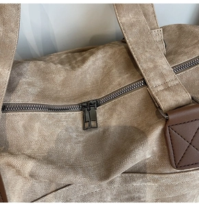 Dettaglio borsa da viaggio in tela kaki con doppia cerniera e rinforzi in pelle marrone