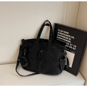 Detail view of black denim tote bag featuring vertical zipper pocket and side pouch