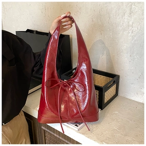 Close-up of a red patent leather tote bag featuring a bow decoration and glossy finish