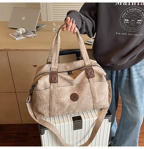 Dettaglio della borsa da viaggio in tela beige con manici in pelle marrone su una valigia