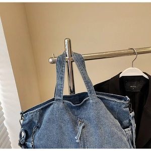 Close-up of blue washed denim tote bag featuring front zipper pocket and metal ring detail