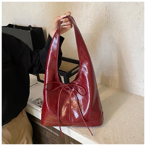 Detail of glossy burgundy tote bag with bow accent and premium mirror finish texture