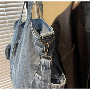 Detail of blue denim tote bag with metal buckle and detachable round coin purse charm