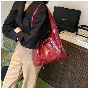Detail of a deep red patent leather shoulder bag with a thin decorative bow tie