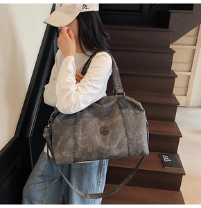 Borsa da viaggio grigio scuro con logo M e tracolla mostrata su una scala in legno