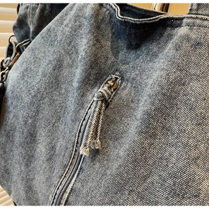 Close-up of blue denim tote bag texture with bronze metal rings and knotted zip puller