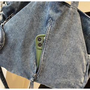 Detailed close-up of denim tote bag with vertical zipper pocket and washed metal hardware