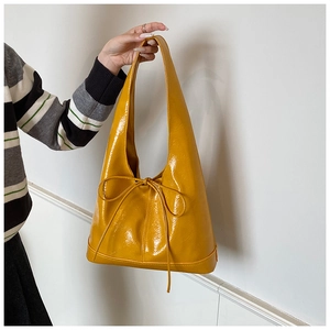 Detail of glossy yellow leather tote bag featuring a decorative bow tie and sleek long handles
