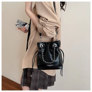 Detail view of a black leather bucket bag featuring a silver chain and adjustable strap