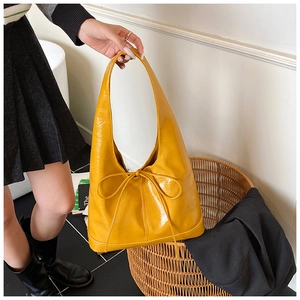 Detail of a bright yellow patent leather tote bag with a bow tie accent for casual daily use