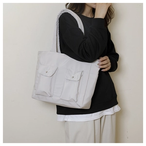 Detail of grey nylon tote bag showing double front flap pockets with metal snap buttons