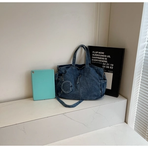 Detail view of denim tote bag with decorative zipper and small round coin purse accessory