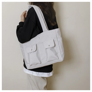 Detail view of large canvas tote bag with front flap pockets and metallic buttons