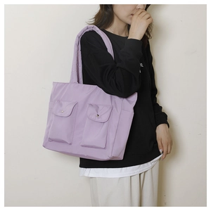 Detail view of large purple nylon tote bag with functional front pockets on a model