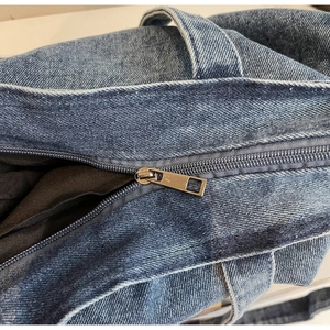 Detailed close-up of the metal zipper and denim texture on the large blue tote bag
