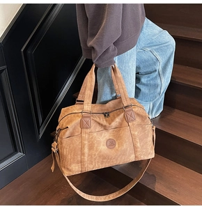 Dettaglio borsa da viaggio marrone vintage con logo in pelle e doppi manici
