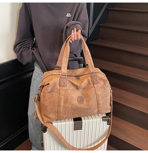 Dettaglio borsa da viaggio in pelle marrone vintage con logo in rilievo e tracolla rimovibile