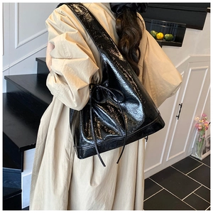 Detail of glossy black hobo bag showing high-shine texture and side drawstring knot detail