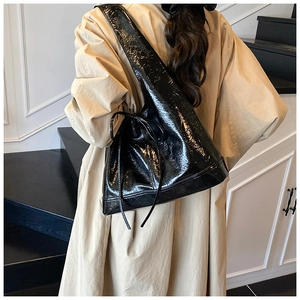 Detail of a large black patent leather hobo bag featuring a decorative bow on shoulder strap