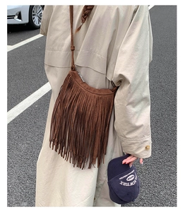 Brown suede bohemian crossbody bag with long tassels shown on shoulder of a model