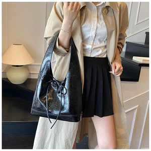 Detail of glossy black tote bag with bow drawstring on a model wearing a trench coat